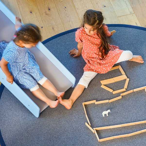 Zwei Kinder spielen auf einem runden Spielteppich.